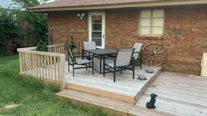 A house with a brick exterior, a wooden deck, a dining table with chairs, and a wheelbarrow.