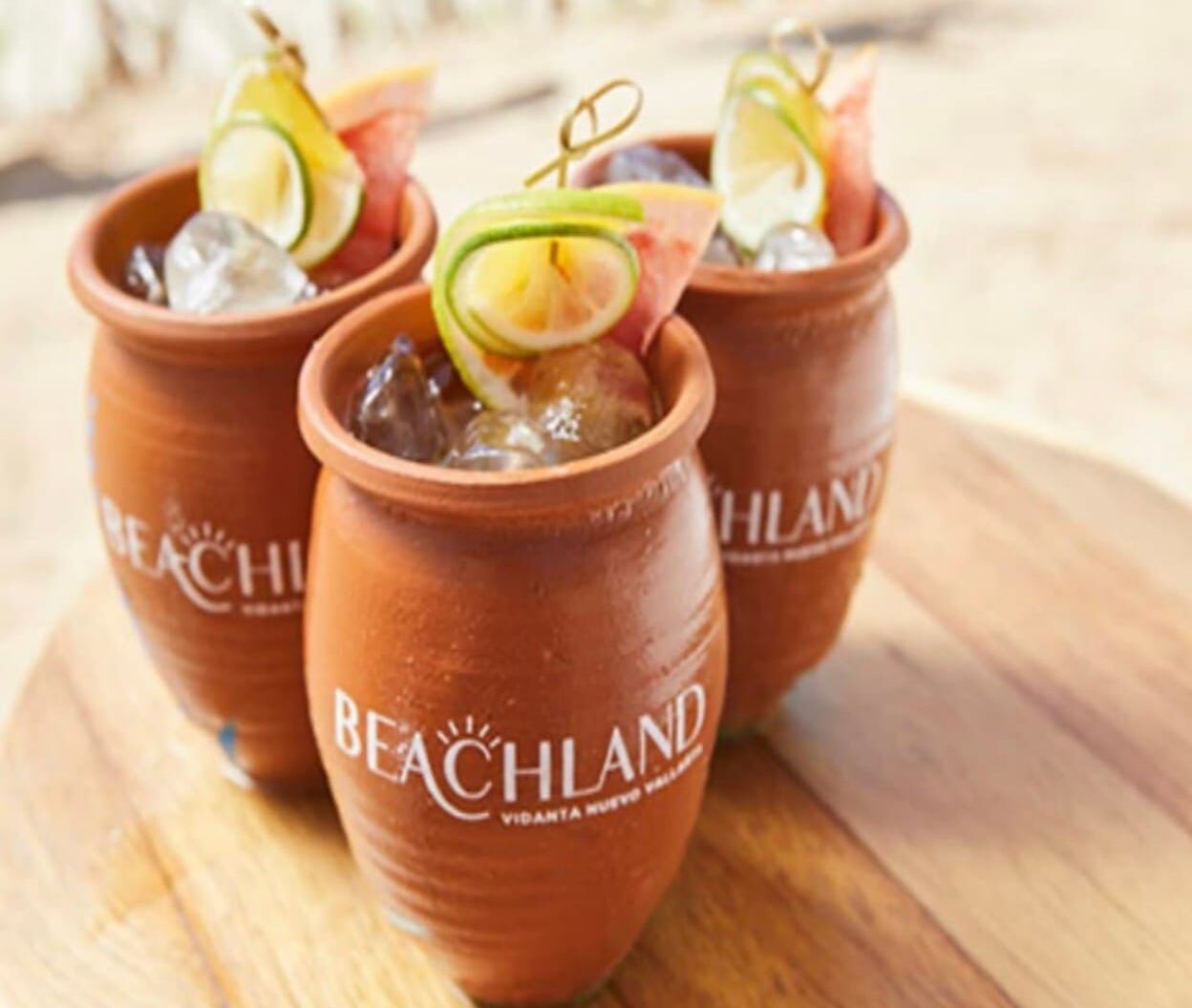 Tres tazas de barro con el logotipo 'Beachland', llenas de hielo y adornadas con rodajas de lima.