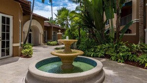 Une cour intérieure avec une fontaine centrale, des palmiers et un bâtiment doté d’un toit en tuiles.
