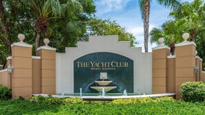 L’entrée privée de la résidence du Yacht Club, agrémentée d’une fontaine et entourée d’une végétation luxuriante et de palmiers.