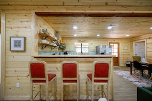 A wooden cabin interior with a kitchen, dining area, and three red upholstered bar stools. - The Swanky Swan Cabin | Secluded Broken Bow Lodge Near Lake, Trails & Hochatown (Hochatown)