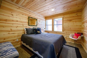 A wooden-paneled bedroom with a bed, a chair, and a window. - The Swanky Swan Cabin | Secluded Broken Bow Lodge Near Lake, Trails & Hochatown (Hochatown)