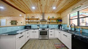 A kitchen with wooden ceiling, white cabinets, a stove, a microwave, and a window. - Whispering Trails Lodge – Secluded Pet-Friendly Broken Bow Cabin | Sleeps 9 | Forest Trails Near Lake & Beavers Bend (Hochatown)
