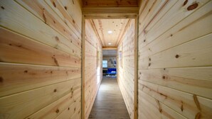 A wooden hallway with a wooden floor, leading to a room with a window and a desk. - Whispering Trails Lodge – Secluded Pet-Friendly Broken Bow Cabin | Sleeps 9 | Forest Trails Near Lake & Beavers Bend (Hochatown)