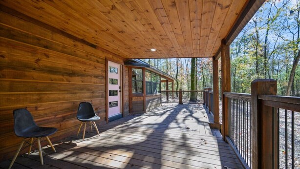A wooden cabin with a porch, two chairs, and a view of the forest. - Whispering Trails Lodge – Secluded Pet-Friendly Broken Bow Cabin | Sleeps 9 | Forest Trails Near Lake & Beavers Bend (Hochatown)