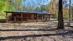 A rustic cabin with a covered porch, surrounded by a forest. - Whispering Trails Lodge – Secluded Pet-Friendly Broken Bow Cabin | Sleeps 9 | Forest Trails Near Lake & Beavers Bend (Hochatown)