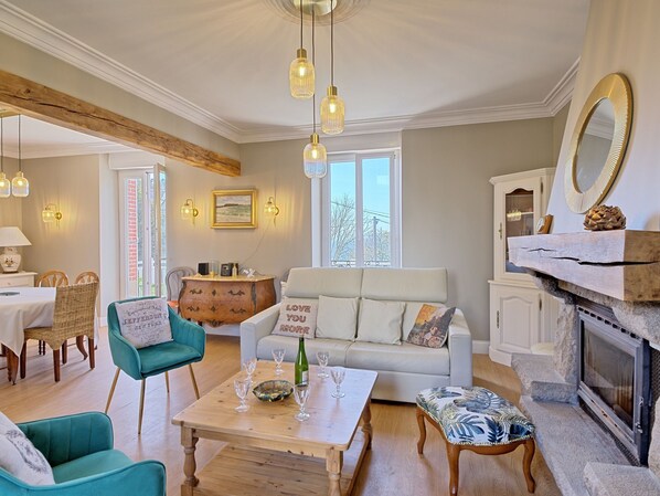 A cozy living room with a fireplace, a sofa, a dining table, and a large window.