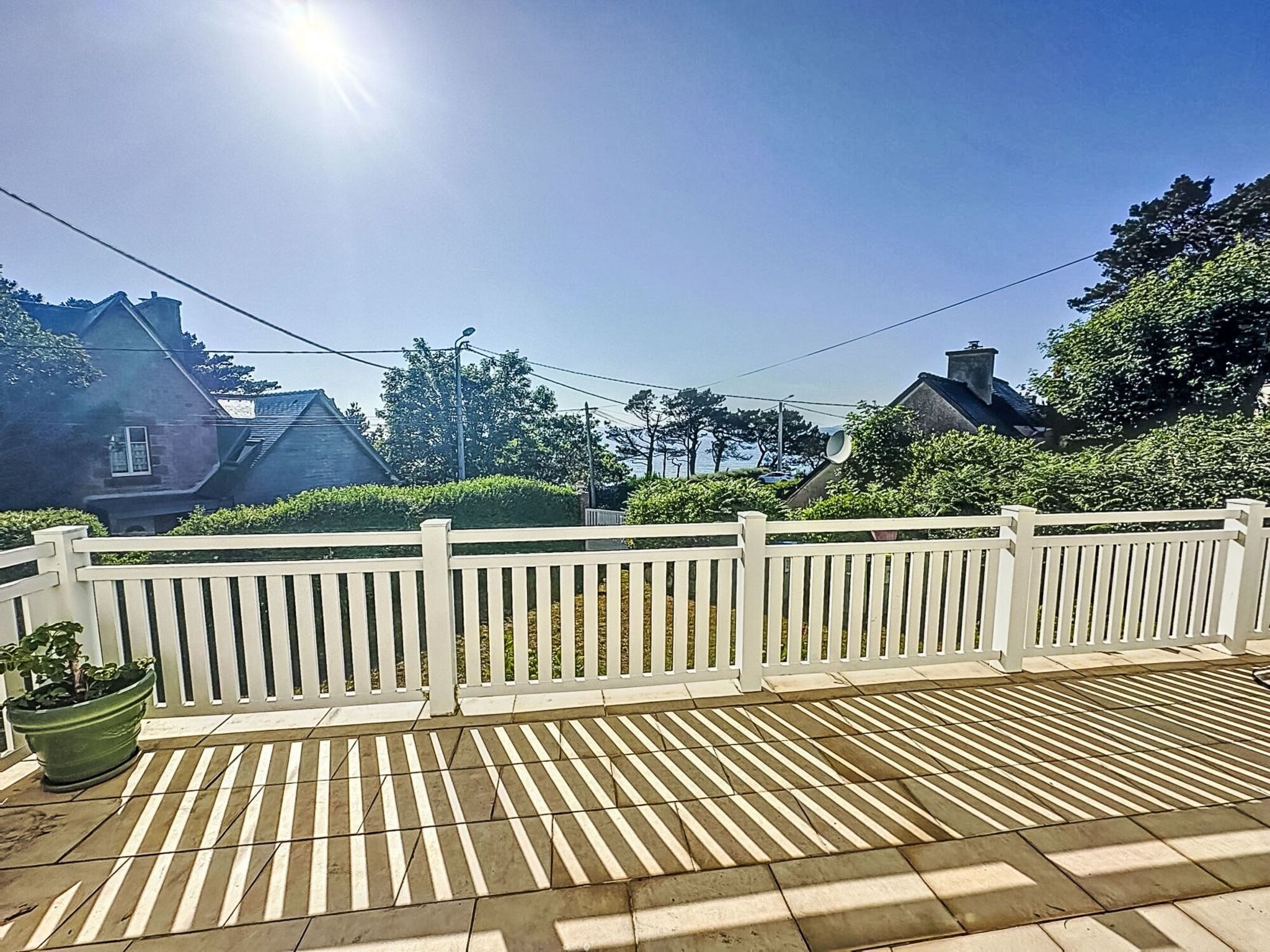 Ein sonniger Außenbereich mit weißem Zaun, einer gefliesten Terrasse und Häusern im Hintergrund.