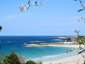 A coastal landscape with a beach, rocky outcrops, and a clear blue sky.
