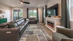 Una sala de estar moderna con un sofá modular, chimenea, televisor de pantalla plana y ventilador de techo.