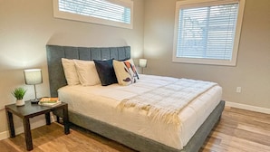 Une chambre à coucher avec un lit, deux tables de chevet, une lampe, une petite plante et une fenêtre avec des stores.