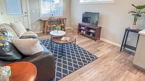 Un salon comprenant un canapé, une table basse, un téléviseur et donnant sur l’extérieur.