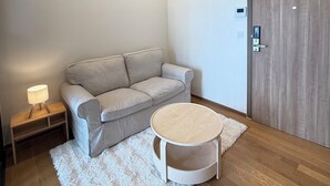 A modern living room with a grey sofa, a round coffee table, a white rug, and a wooden door.