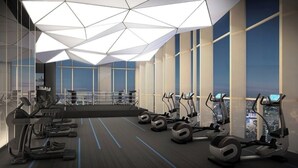 A modern gym with treadmills, stationary bikes, and elliptical machines arranged in rows with large windows offering city views.