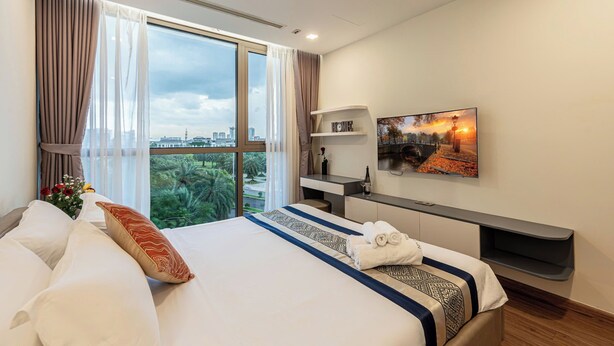 A hotel room with a large bed, a TV mounted on the wall, a desk, and a window with curtains. - Apartment in Landmark-Vinhome.CTP by Yen (Ho Chi Minh City)