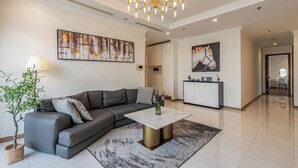 A modern living room with a grey sectional sofa, a white coffee table, and a chandelier. - Apartment in Landmark-Vinhome.CTP by Yen (Ho Chi Minh City)