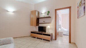 A modern living room with a TV, wooden cabinet, and a small table with a lamp. - GuestHost - La Mole Apartment with Balcony (Torino)