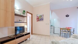 A modern living room with a flat-screen TV, wooden entertainment unit, and a dining area with a table and chairs. - GuestHost - La Mole Apartment with Balcony (Torino)