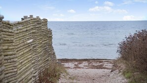A coastal path leading to the sea, bordered by a stone wall and sparse vegetation.