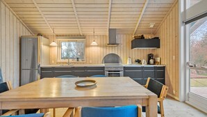 A modern kitchen with wooden walls, a large window, and a dining area with a wooden table and blue chairs.