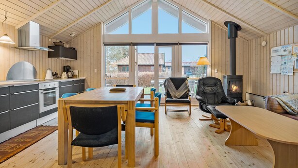 A spacious kitchen with a large dining table, a black leather chair, and a wood-burning stove.