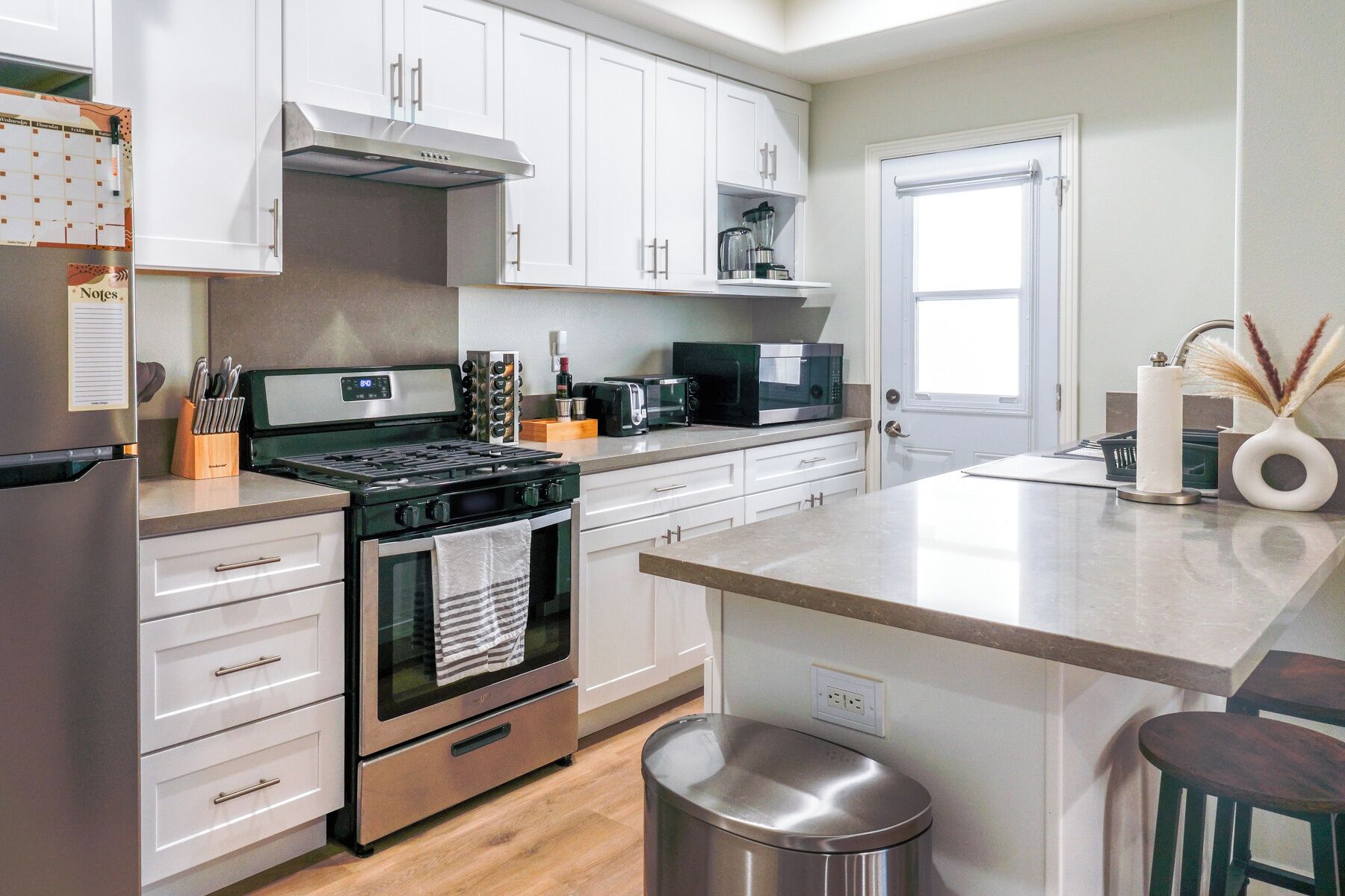 A modern kitchen with white cabinets, a stainless steel stove, a microwave, and a toaster.