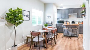 Une cuisine moderne avec des meubles de couleur grise, une table à manger en bois avec quatre chaises, et un coin bar avec des tabourets.