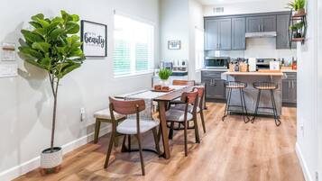 A modern kitchen with grey cabinets, a wooden dining table with four chairs, and a bar area with stools.
