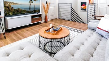 A modern living room with a flat-screen TV, a round coffee table, and a tufted sofa.