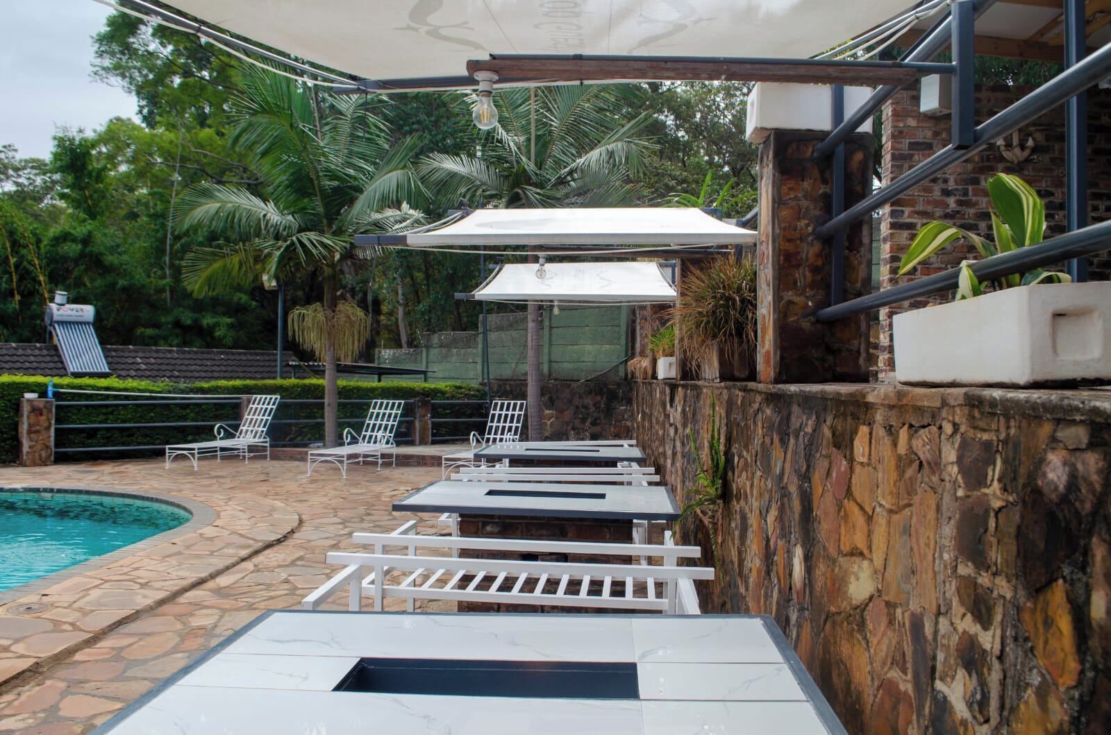 A poolside area with lounge chairs, a stone wall, and a covered seating area.