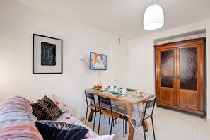 A living room with a sofa, a dining table with chairs, a television, and a wooden cabinet.