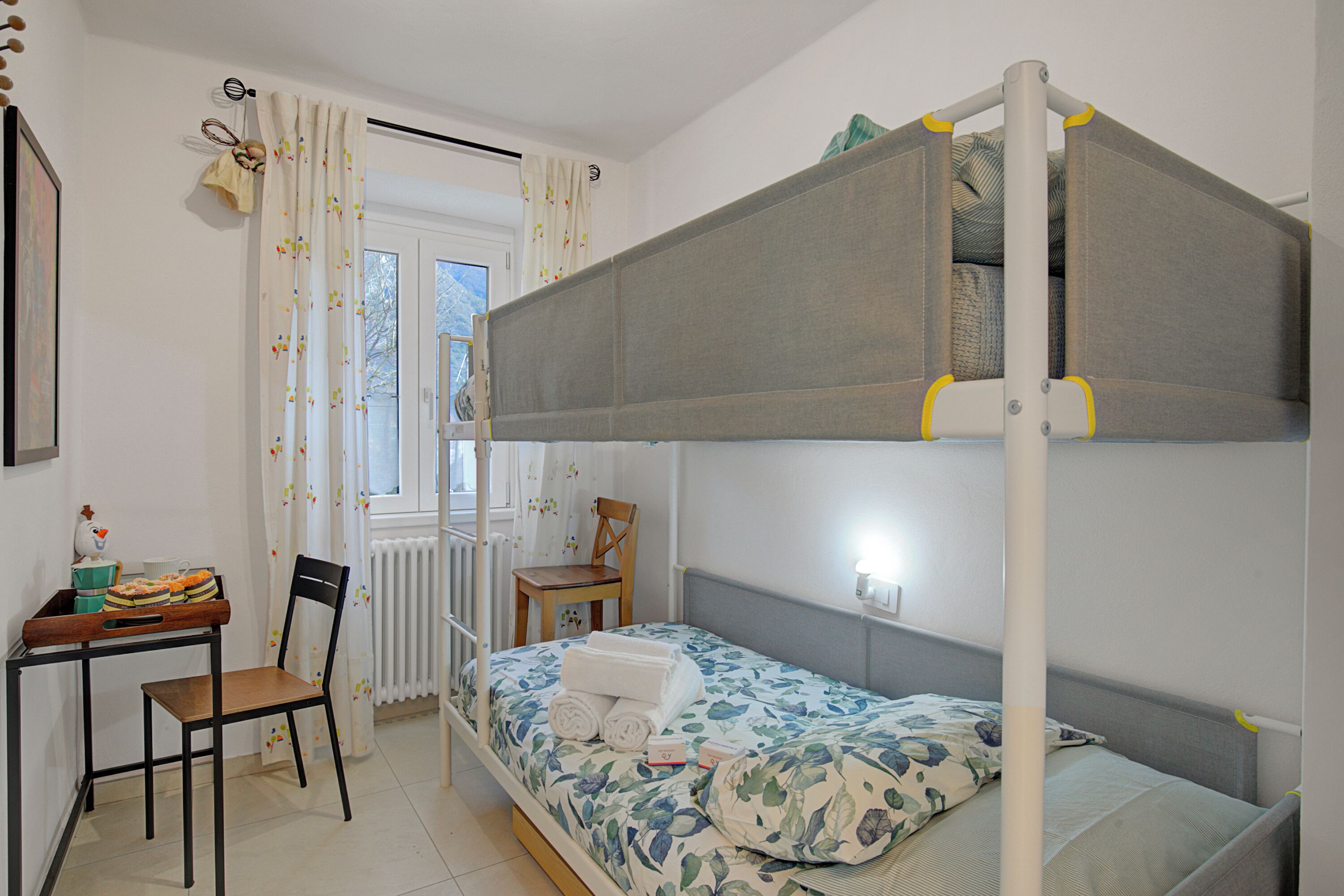 A bunk bed with a desk and chair, a radiator, and a window with curtains.