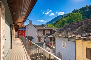 A balcony overlooking a village with traditional stone buildings, a clear sky, and a mountain in the background.