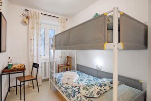 A bunk bed with a desk and chair, a radiator, and a window with curtains.