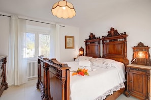 A traditional bedroom with a wooden bed, a radiator, a window with curtains, and a wall-mounted picture. - Casa del Nildo near Mountain and Lake Mergozzo, Ornavasso, Italy (Ornavasso)