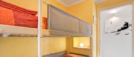 A bunk bed room with a reading light, a door with a black and white artwork, and a wooden floor.