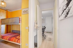 Una stanza con un letto a castello, un muro giallo e una porta che conduce a un'altra stanza con un tavolo e sedie da pranzo.