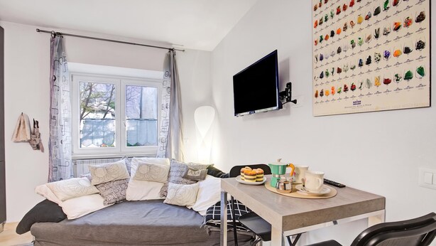 Une chambre moderne comprenant un lit, un téléviseur, un coin repas avec une table et des chaises, et un mur orné d’une collection de minéraux.