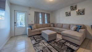 Een woonkamer met een beige modulaire bank, een passende voetenbankje, een vloerkleed met patroon en een plafondlamp.