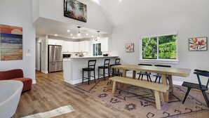 Une cuisine moderne avec des meubles blancs, un réfrigérateur en acier inoxydable et un coin repas comprenant une table et des chaises en bois.