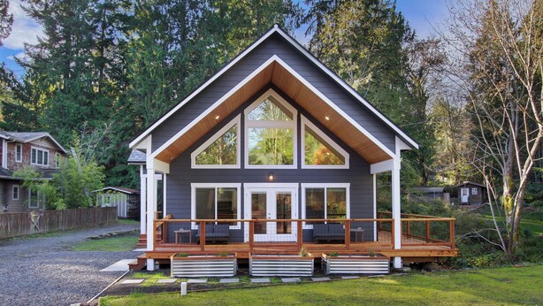 Une cabane moderne à deux étages, dotée d’une terrasse en bois, de grandes fenêtres et d’un porche abrité.