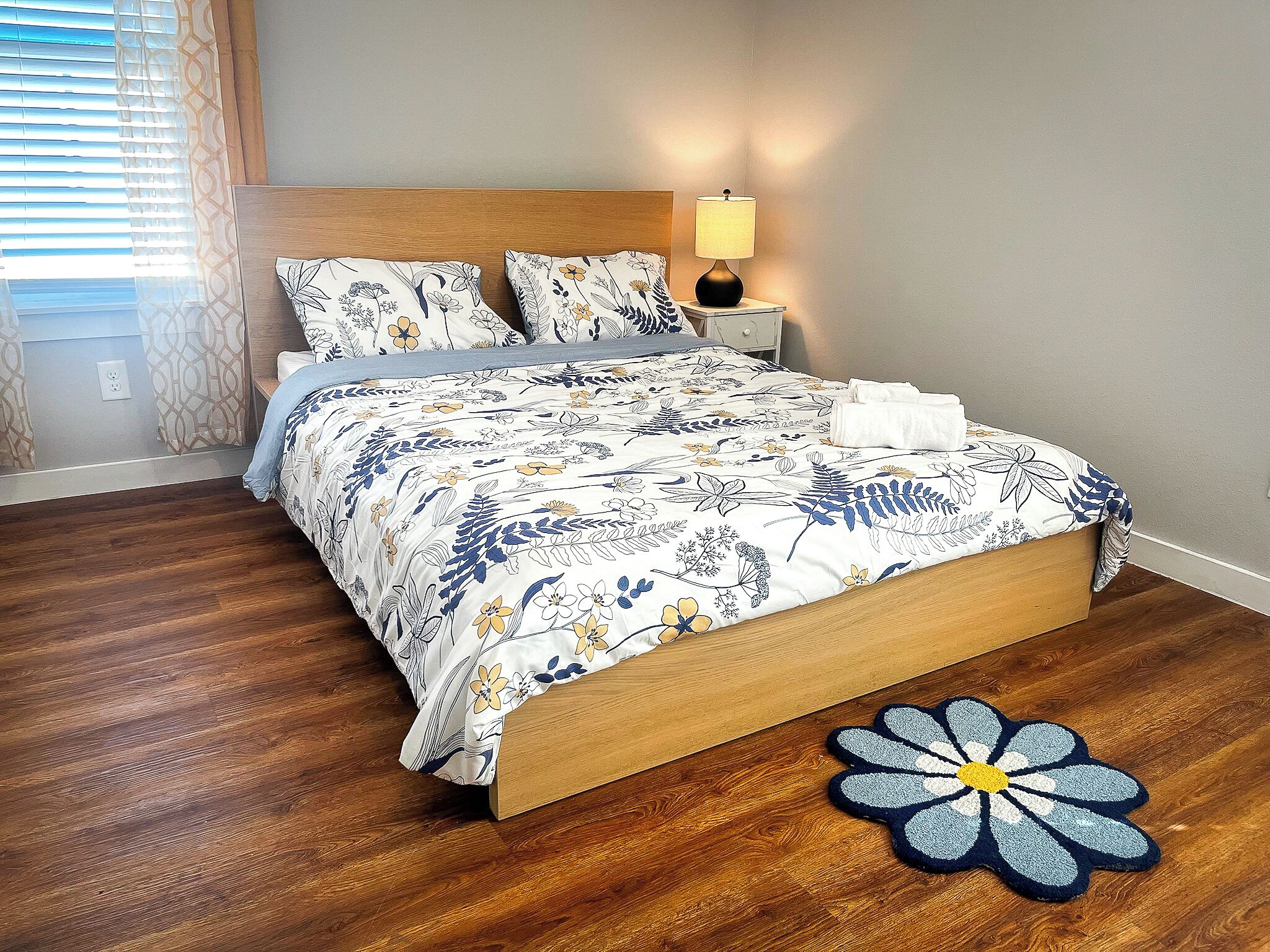 A neatly made bed with floral bedding, a bedside lamp, and a wooden headboard.