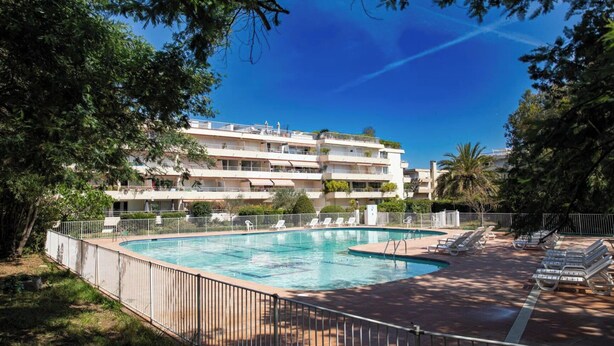 Una piscina con lettini, circondata da una recinzione, e un edificio a più piani sullo sfondo.