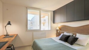 Una camera da letto con un letto, una scrivania, una sedia, una finestra e vista sugli edifici.