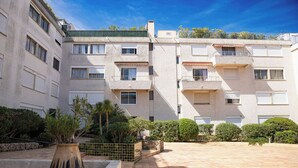 Un edificio residenziale a più piani con balconi, un cortile lastricato e vegetazione circostante.