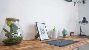 Una scrivania in legno con un codice QR incorniciato, una piccola pianta in vaso, una bottiglia verde, una statua di Buddha e una lampada da tavolo.