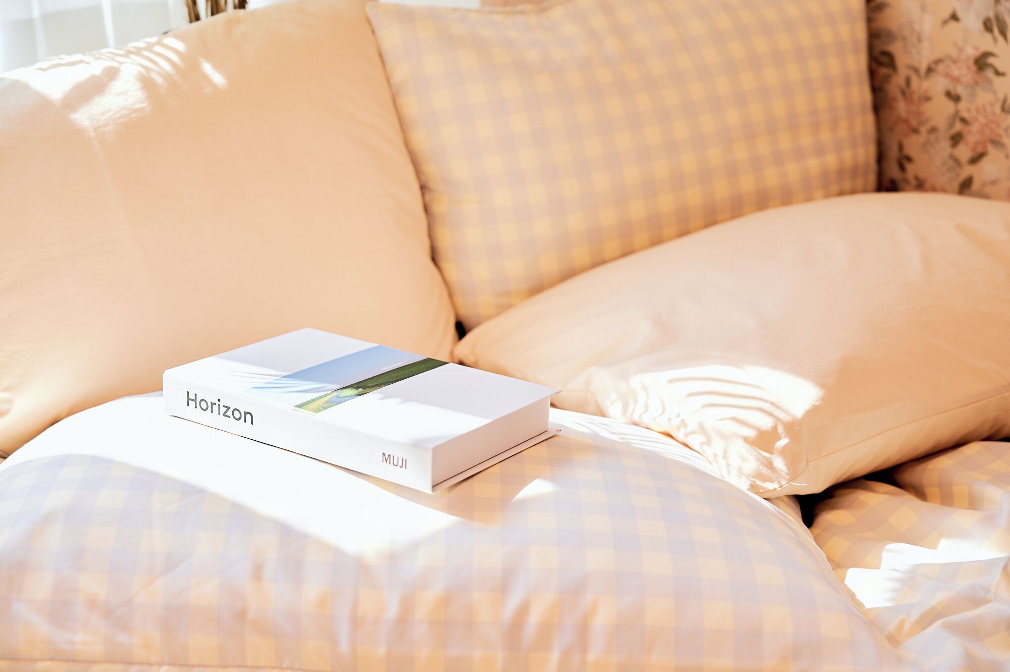 Eine weiße Horizon MUJI Box auf einem Bett mit karierter Bettwäsche.