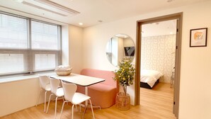 A modern room with a wooden floor, a white table with chairs, a pink sofa, a mirror, and a bed with a floral wallpaper. - Maison de Wave 3 (Seoul)