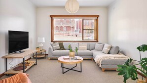 Ein Wohnzimmer mit einer Couch, einem Couchtisch, einem Fernseher und einem großen Fenster mit Jalousien.