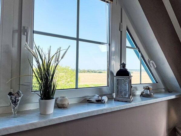 A window with a view of a field, a potted plant, and decorative items on the sill.